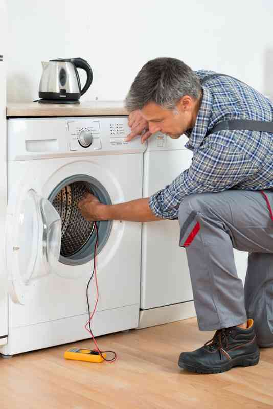 Full length of repairman checking washing machine with digital multimeter at home